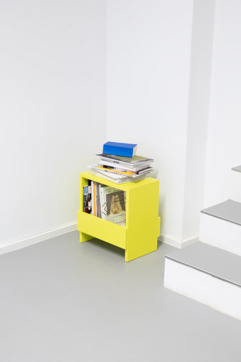 Ein Hocker oder Beistelltisch aus Massivholz mit Stauraum in schwefelgelb gefüllt mit Büchern und Zeitschriften