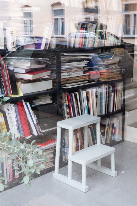 Tritt-Hocker Adhoc in grau als Bibliotheksleiter vor einem gefüllten Bücherregal