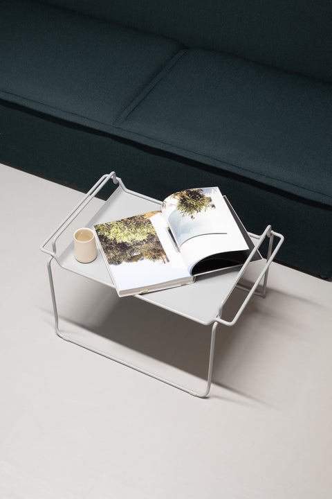 Couchtisch Tanges vor einem dunkelgrünen Sofa mit einem aufgeschlagenem Buch und einer Tasse